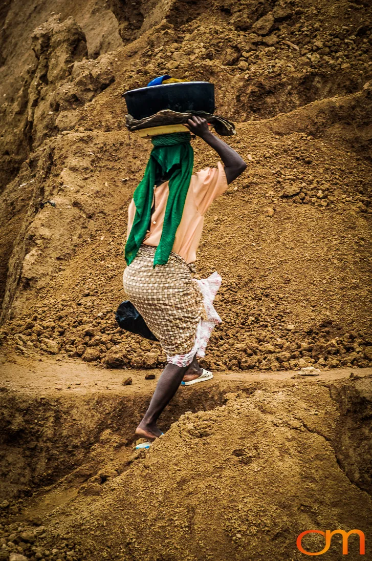 Basin balanced on her head, a woman climbs a bank of excavated sand