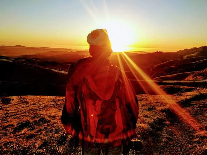 Amanda Fornal, seen from behind with a backpack, watching the sun set over rolling hills.