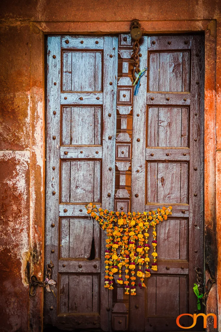 Marigold garland hung on a weathered wooden double door in an ochre wall